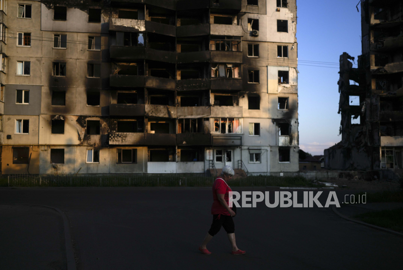 Seorang wanita berjalan di depan sebuah bangunan yang dihancurkan oleh serangan, di Borodyanka, di pinggiran Kyiv, Ukraina, Minggu, 12 Juni 2022.