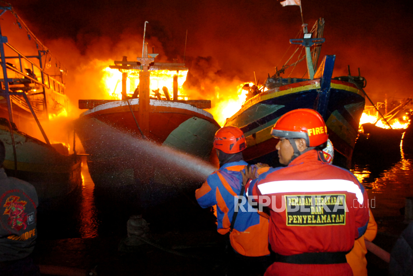 Petugas pemadam kebakaran berusaha memadamkan api yang membakar kapal nelayan, di Pelabuhan Jongor, Tegal, Jawa Tengah, Senin (14/8/2023) malam. Pemadam kebakaran dan warga kesulitan memadamkan api akibat angin besar dan banyak oli di atas kapal.  