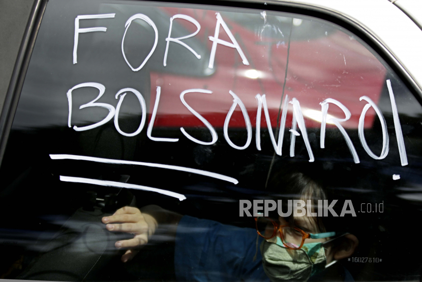  Seorang anak laki-laki mengendarai kendaraan dengan teks dalam bahasa Portugis di jendela yang bertuliskan Bolsonaro Out! selama protes terhadap tanggapan pemerintah dalam memerangi COVID-19 dan menuntut pemakzulan Presiden Brasil Jair Bolsonaro, di Brasilia, Brasil, Sabtu, 21 Februari 2021.