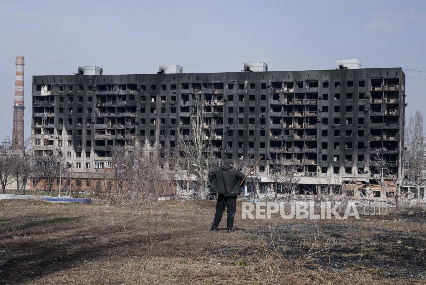 Seorang pria melihat gedung apartemen yang terbakar yang dirusak oleh penembakan di Mariupol, Ukraina. Perang Rusia dan Ukraina bisa berdampak terhadap perekenomian Indonesia 