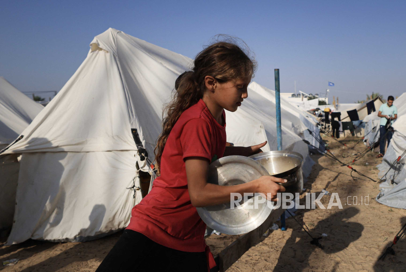 Seorang gadis muda membawa makanan yang didistribusikan di kamp darurat bagi para pengungsi di Khan Yunis di Jalur Gaza selatan pada (25/10/2023.