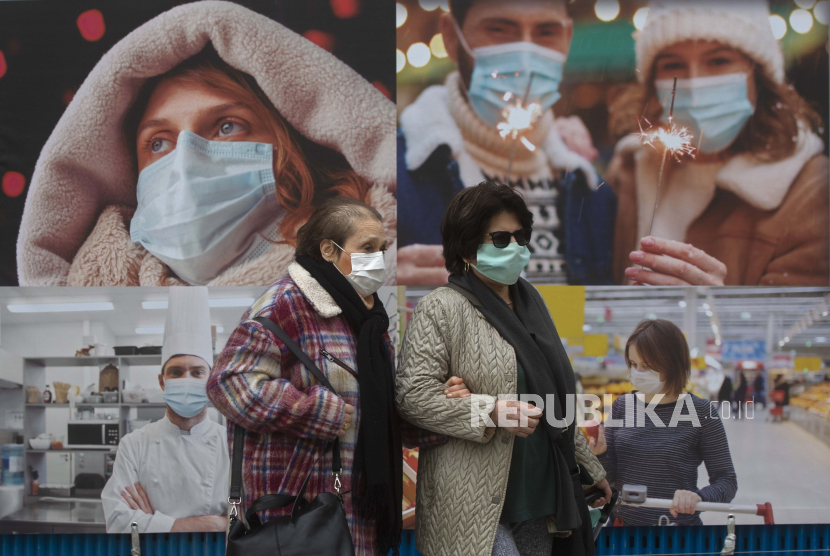 Dua perempuan memakai masker wajah untuk melindungi dari penyebaran virus corona, berjalan melewati poster di jalan di Madrid, Spanyol, Kamis, 17 Desember 2020. Beberapa wilayah Spanyol memperketat pembatasan kesehatan untuk liburan Natal dengan kasus baru COVID-19. sudah bangkit kembali.
