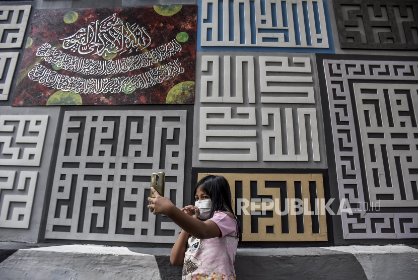 A child takes a selfie in front of a calligraphy mural in the Calligraphy Cultural Tourism Village, Kiaracondong District, Bandung City.