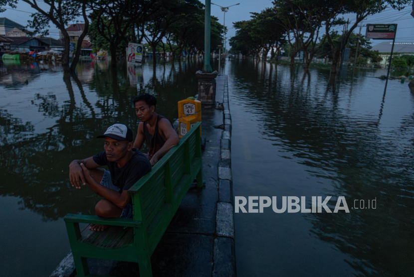 Warga duduk di pembatas jalan yang tergenang banjir di jalur pantura Demak-Kudus, Kecamatan Karanganyar, Kabupaten Demak, Jawa Tengah, Rabu (14/2/2024). 