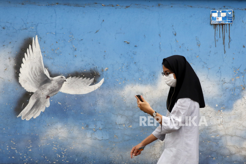  Seorang warga Iran yang mengenakan masker wajah berjalan di jalan di Teheran, Iran, ilustrasi