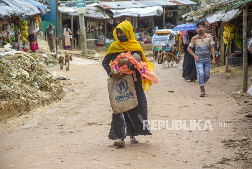 Seorang ibu pengungsi Rohingya dengan bayinya berjalan di jalan di sepanjang kamp darurat.