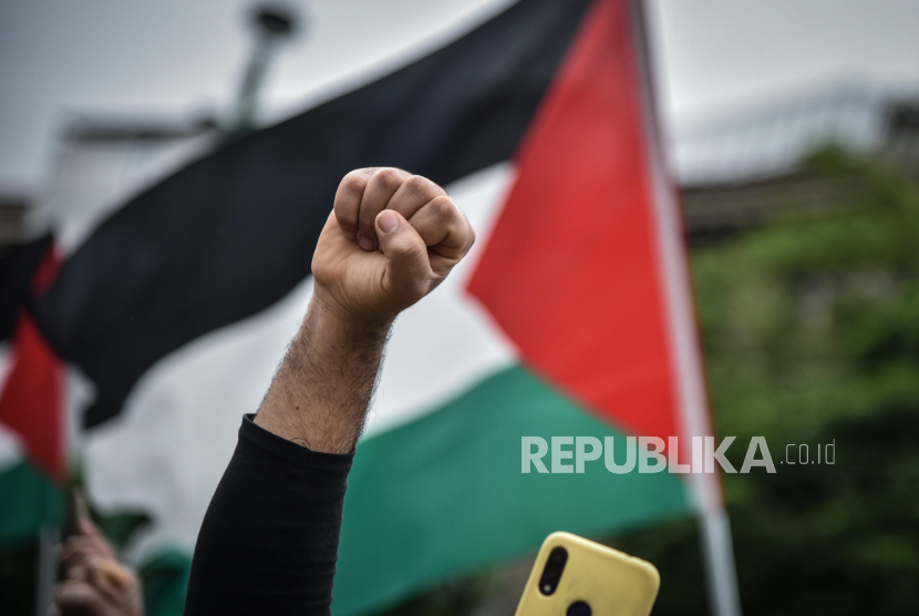 Seorang peserta mengepalkan tangan di depan bendera Palestina saat demonstrasi di Milan menentang eskalasi kekerasan antara Palestina dan Israel, di Milan, Italia, 16 Mei 2021.