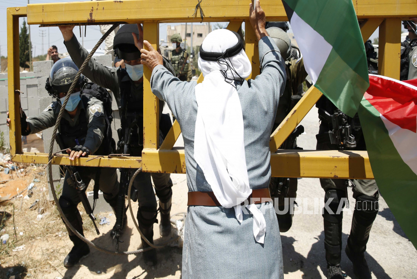 Pemrotes Palestina memegang bendera Palestina ketika ia berdebat dengan tentara Israel ketika mereka mencoba untuk mencapai tanah mereka selama demonstrasi menentang rencana Israel untuk mencaplok bagian-bagian Tepi Barat yang diduduki di desa Hares dekat kota Salfit di Tepi Barat utara, 24 Juli 2020. 