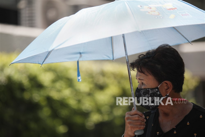 Warga memakai payung untuk melindungi diri dari =sinar matahari saat cuaca panas.