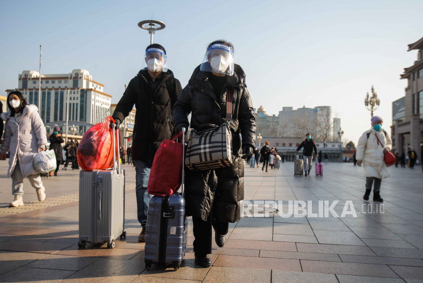 Passengers wearing face masks walk with their luggage in front of the Beijing Railway Station in Beijing, China, 10 January 2023. Chinese passengers are travelling domestically as the nation