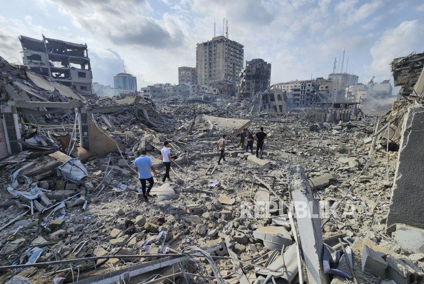 Warga Palestina berjalan melewati puing-puing bangunan yang hancur akibat serangan udara Israel di Kota Gaza.
