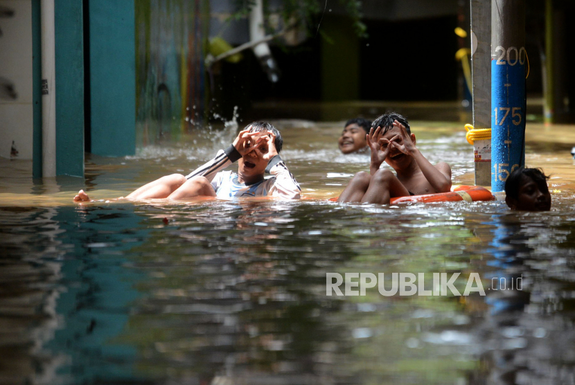 Anak-anak berenang ketika banjir merendam di kawasan Kebon Pala, Kampung Melayu, Kecamatan Jatinegara, Jakarta Timur, Senin (27/2/2023).