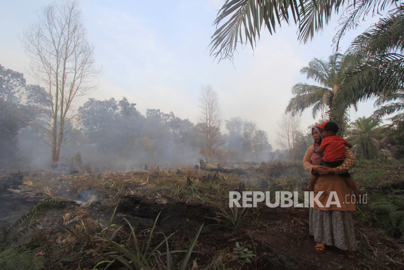 Petani menggendong anaknya saat melihat kebun nanas yang ikut terbakar di Kecamatan Medang Kampai, Dumai, Riau, Senin (22/2/2021). Kebakaran lahan gambut seluas 11 hektar yang menjalar ke perkebunan warga tersebut disebabkan cuaca panas selama tiga pekan terakhir. 