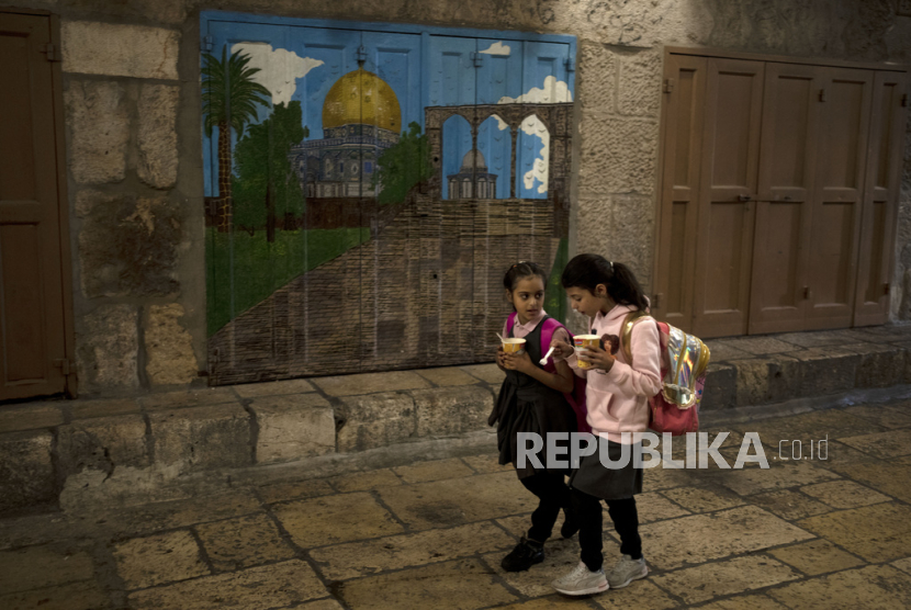 Dua anak perempuan Palestina makan mie saat mereka berjalan pulang dari sekolah melalui deretan etalase toko yang ditutup untuk pemogokan umum yang menyerukan gencatan senjata di Gaza, di Kota Tua Yerusalem, Palestina, Senin (11/12/2023).