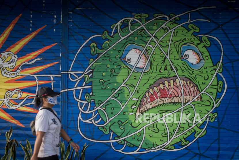 Warga melintas di depan mural bertema Covid-19 di Kemplayan, Solo, Jawa Tengah. Senin (15/3), menandai satu tahun sejak Presiden Joko Widodo menyerukan masyarakat untuk bekerja, belajar, dan beribadah dari rumah. 