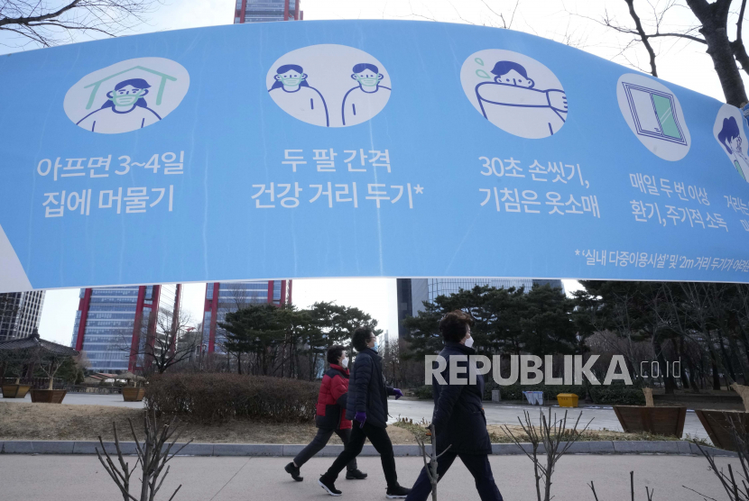 Orang-orang yang memakai masker melewati spanduk yang mengingatkan tindakan pencegahan terhadap virus corona di sebuah taman di Seoul, Korea Selatan, Senin, 24 Januari 2022.