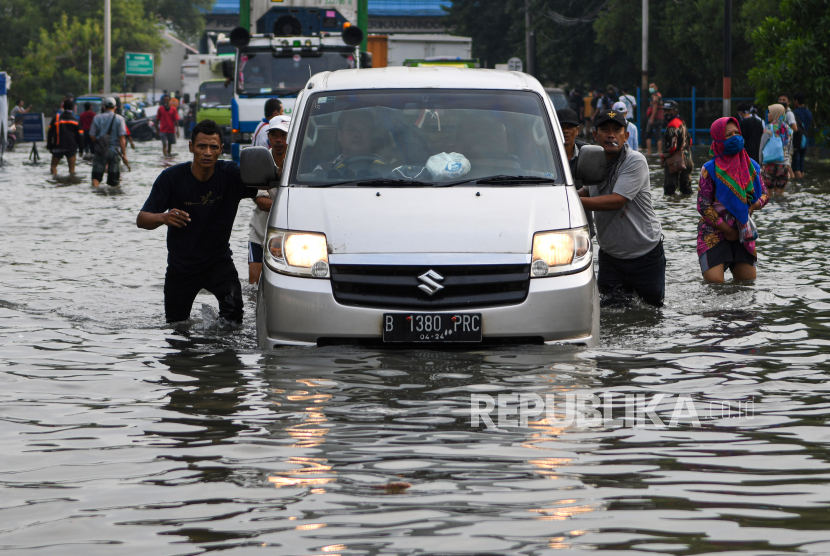 Warga mendorong mobil yang mogok saat melintasi banjir air rob di kawasan Muara Baru, Penjaringan, Jakarta Utara.