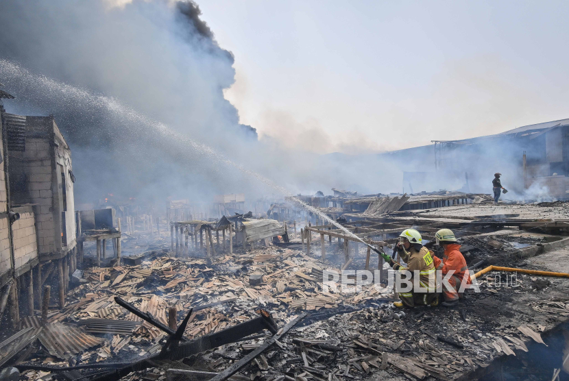 Petugas pemadam kebakaran berusaha memadamkan api saat kebakaran permukiman padat penduduk di Kapuk Muara, Jakarta, Ahad (30/7/2023). Kebakaran tersebut juga merambat ke pergudangan yang berada dekat permukiman warga. 