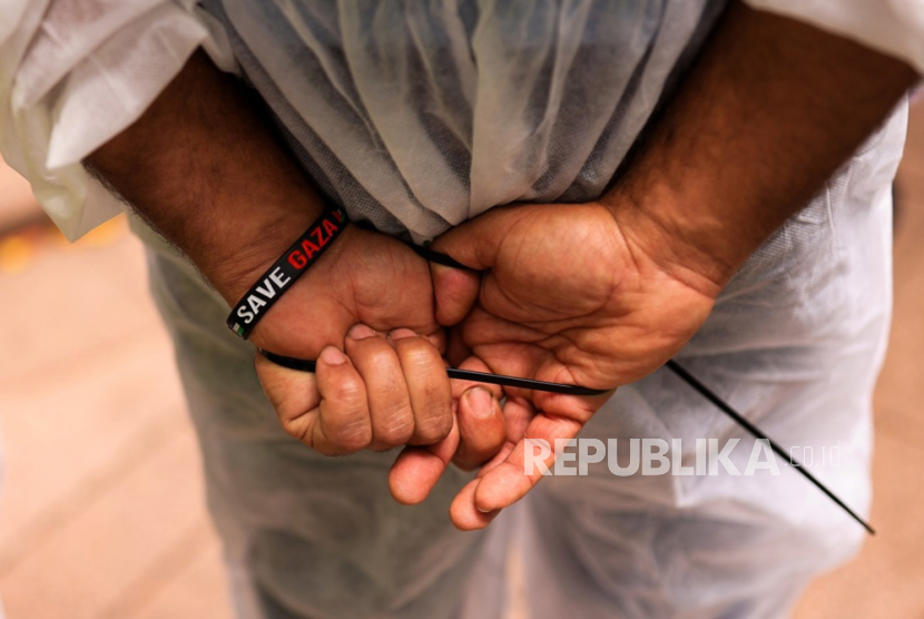 Tangan seorang pengunjuk rasa yang berpakaian seperti tahanan Palestina terlihat diborgol plastik.
