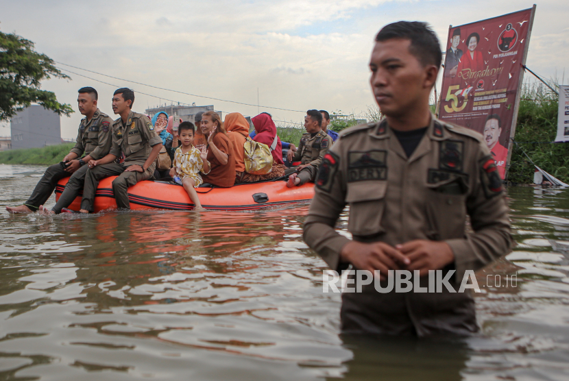 Petugas mengangkut warga menggunakan perahu karet di tengah banjir.