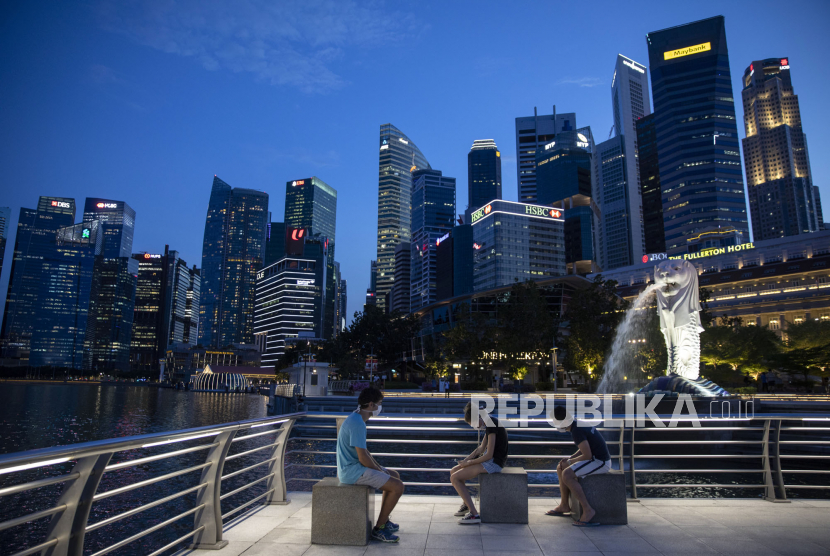 Pengunjung mengenakan masker duduk di Taman Merlion, Singapura, Rabu (15/4). Singapura pada Jumat akan mencabut sebagian aturan pembatasan.