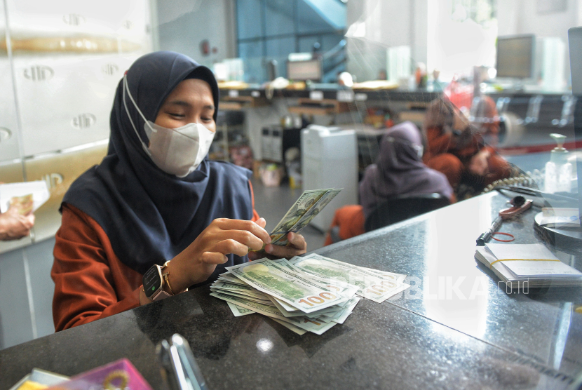 Petugas menghitung uang dollar AS di tempat penukaran valuta asing.