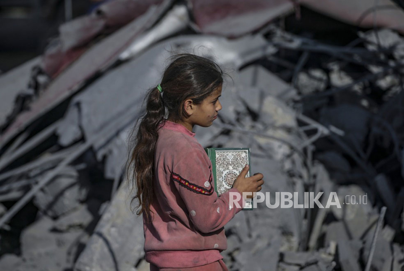Seorang gadis muda memegang mushaf Al-Quran di lokasi masjid Al Bokhari yang hancur menyusul serangan udara Israel di Deir Al Balah, Jalur Gaza selatan, (2/3/2024).