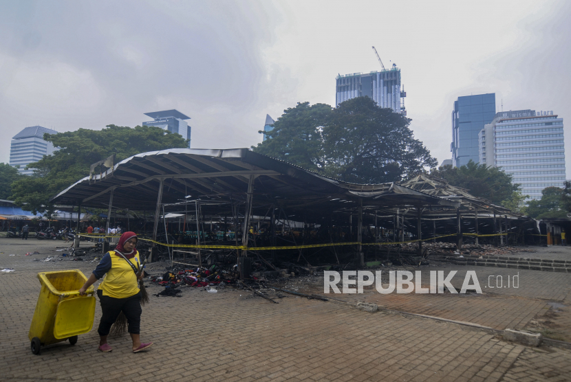 Petugas kebersihan berjalan di dekat puing-puing kios pasca kebakaran di kawasan Monas, Jakarta. Pemprov DKI menargetkan untuk kembali membangun kios terbakar di Monas usai lebaran.