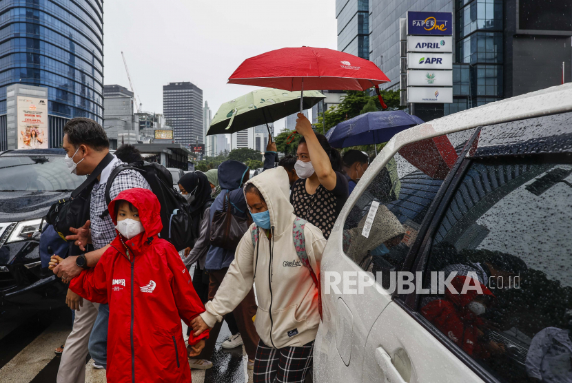 Orang-orang melintasi jalan yang sibuk di bawah hujan di Jakarta, Indonesia, 28 Desember 2022. Wapres mengimbau masyarakat berhati-hati dalam berwisata di tengah cuaca ekstrem.