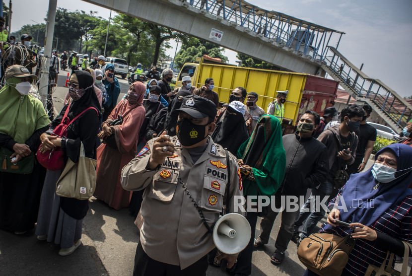 Petugas Kepolisian mengimbau kepada massa pendukung untuk menjaga jarak saat berlangsungnya sidang lanjutan kasus pelanggaran protokol kesehatan dengan terdakwa Rizieq Shihab di Pengadilan Negeri (PN) Jakarta Timur, Jakarta, Jumat (19/3/2021). Sidang tersebut beragendakan pembacaan dakwaan dari Jaksa Penuntut Umum (JPU). 
