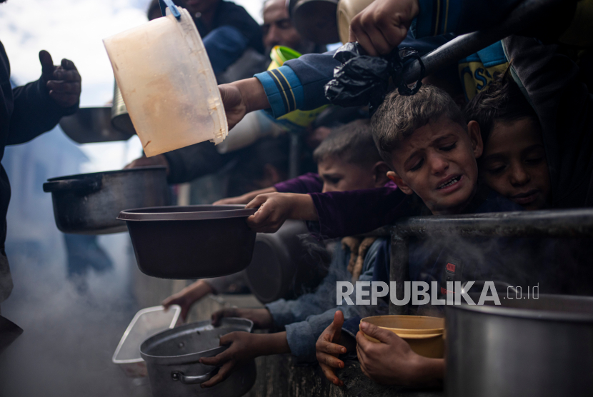 Anak-anak dan warga Palestina antre untuk mendapatkan makanan gratis di Rafah, Jalur Gaza, Jumat (16/2/2024). Badan bantuan internasional mengatakan Gaza menderita kekurangan makanan, obat-obatan, dan pasokan pokok lainnya akibat perang antara Israel dan Hamas.