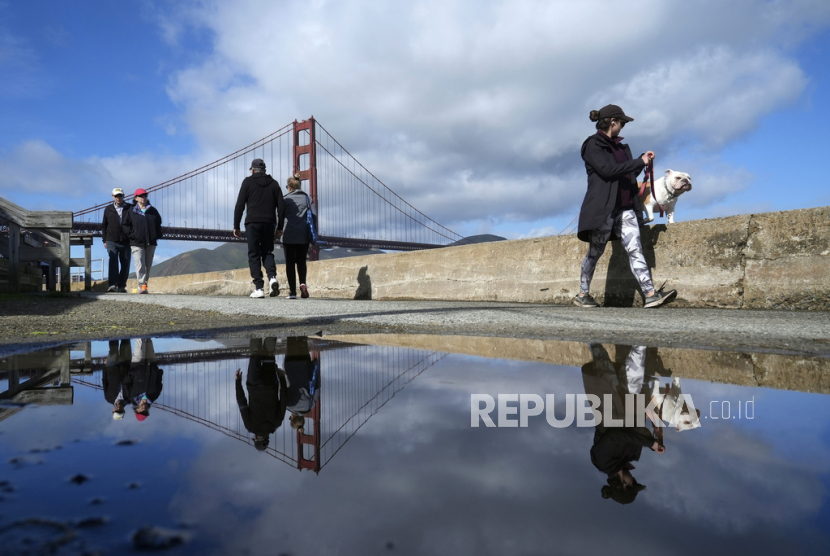 Pejalan kaki dan menara Jembatan Golden Gate terpantul di genangan air dekat Crissy Field di San Francisco, Kamis, 8 Februari 2024.
