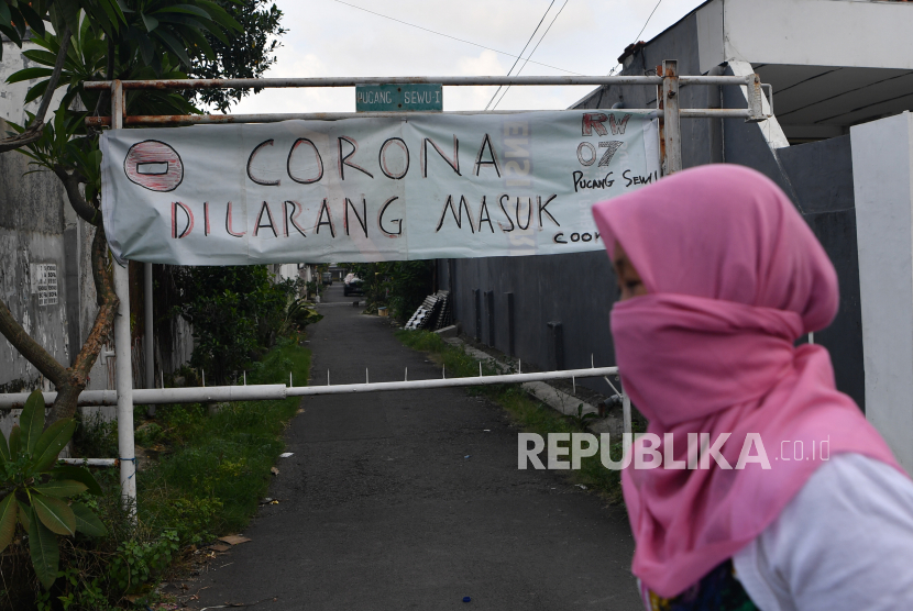 Warga melintas di depan pintu masuk Kampung Pucang Sewu yang melakukan karantina wilayah, Surabaya, Jawa Timur, Minggu (5/4/2020). Karantina wilayah tersebut dilakukan oleh warga di kampung itu guna mencegah penyebaran Virus Corona (COVID-19)