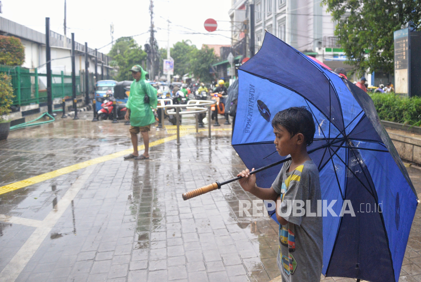 Seorang anak menawarkan jasa ojek payung kepada warga di Stasiun Tebet, Jakarta, Selasa (30/1/2024). 