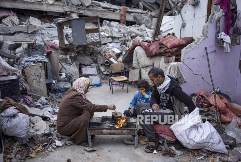 Anggota keluarga Al-Rabaya berbuka puasa selama bulan suci Ramadhan di luar rumah mereka yang hancur akibat serangan udara Israel di Rafah, Jalur Gaza, Senin, (18/3/2024).
