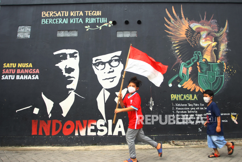 Dua bocah berlari mengibarkan bendera merah putih.