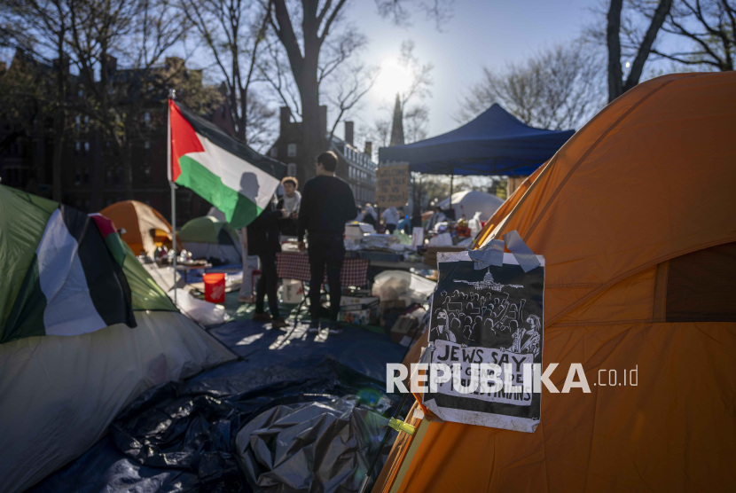 Students protesting against the war in Gaza stand next to a Palestinian flag and tents at an encampment in Harvard Yard, at Harvard University in Cambridge, Mass., on Thursday, April 25, 2024.  