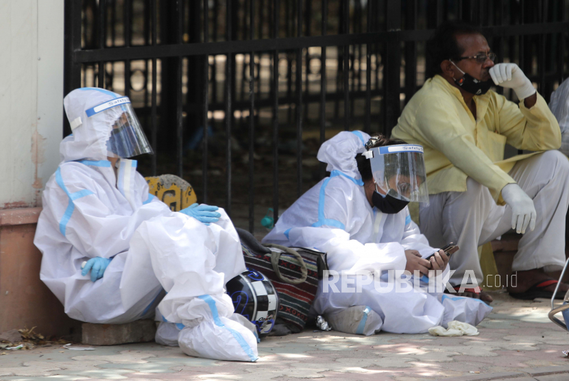 Orang-orang dengan pakaian pelindung pribadi menunggu di luar kamar mayat untuk mengambil jenazah kerabat mereka yang meninggal karena virus corona, di New Delhi, India, Senin, 19 April 2021. 