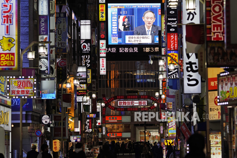  Orang-orang berjalan saat siaran publik menunjukkan Perdana Menteri Jepang Yoshihide Suga mengumumkan keadaan darurat selama konferensi pers yang disiarkan televisi di Tokyo, Jepang, 07 Januari 2021. 