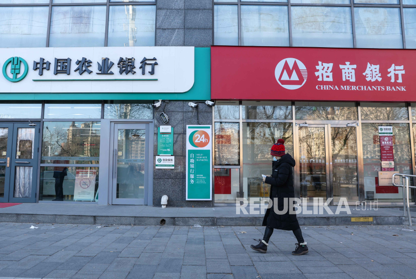   Seorang wanita yang mengenakan masker berjalan di samping bank di Beijing, Tiongkok, 22 Januari 2024. Bank Sentral China menurunkan suka bunga KPR 25 basis poin, Selasa (20/2/2024).