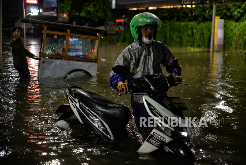 Pengendara mendorong motornya saat menerobos banjir di Jalan Kemang Raya, Jakarta Selatan, Selasa (5/10/2022). Wagub DKI Riza Patria sebut sumur resapan berperan penting dalam menangani banjir.