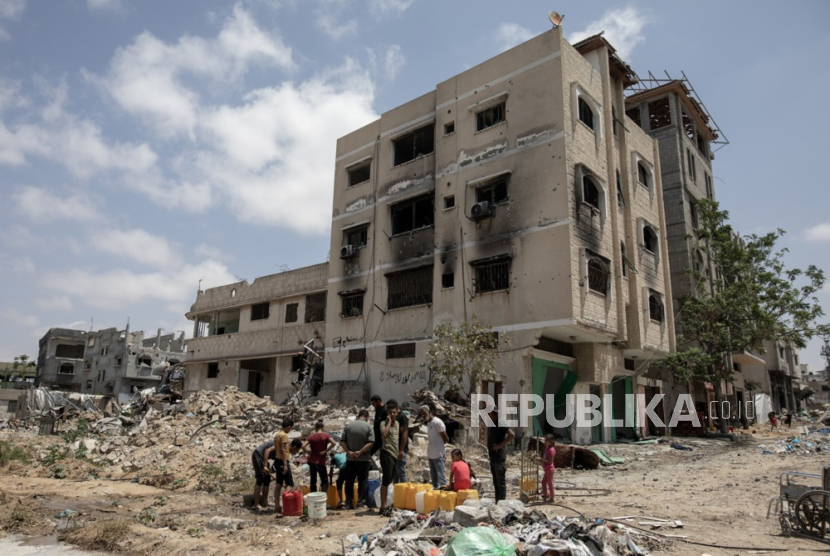 Warga Palestina mengisi botol dengan air dari pipa bawah tanah di samping bangunan yang hancur di Khan Yunis setelah tentara Israel menarik pasukannya dari Jalur Gaza selatan, (2/5/2024).