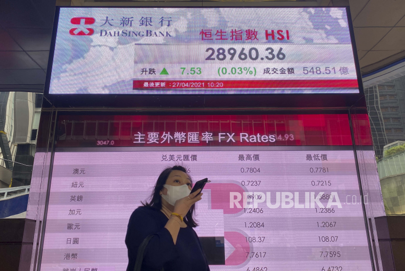 Seorang wanita berjalan melewati papan elektronik bank yang menunjukkan indeks saham Hong Kong di Bursa Efek Hong Kong Selasa, 27 April 2021. 