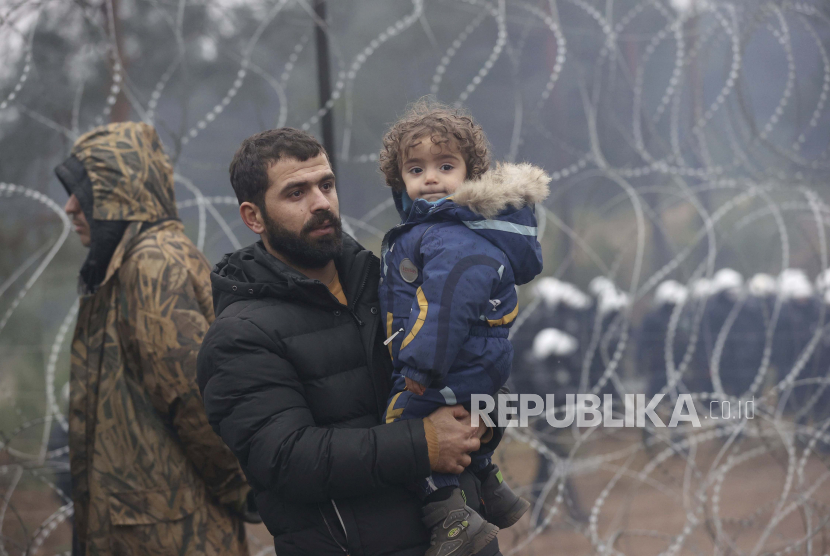 Muslim Kuburkan Migran di Perbatasan Belarusia-Polandia. Seorang migran dengan seorang anak berjalan di sepanjang pagar kawat berduri ketika yang lain berkumpul di perbatasan Belarus-Polandia dekat Grodno, Belarus,14 November 2021. 