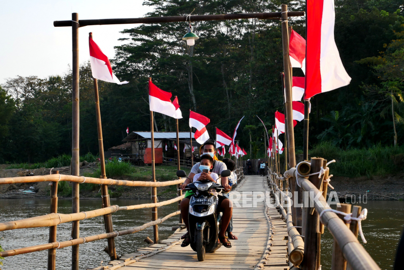 Warga memanfaatkan jembatan sesek atau jembatan bambu bertema kemerdekaan di Lendah, Kulonprogo, Yogyakarta. Masyarakat diminta untuk mengibarkan bendera Merah Putih mulai 1 Agustus ini.
