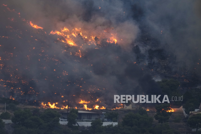 Api mendekati rumah-rumah di Kalamaki dekat Agioi Theodori sekitar 60 Kilometer sebelah barat Athena, Yunani, Selasa, (18/7/2023).