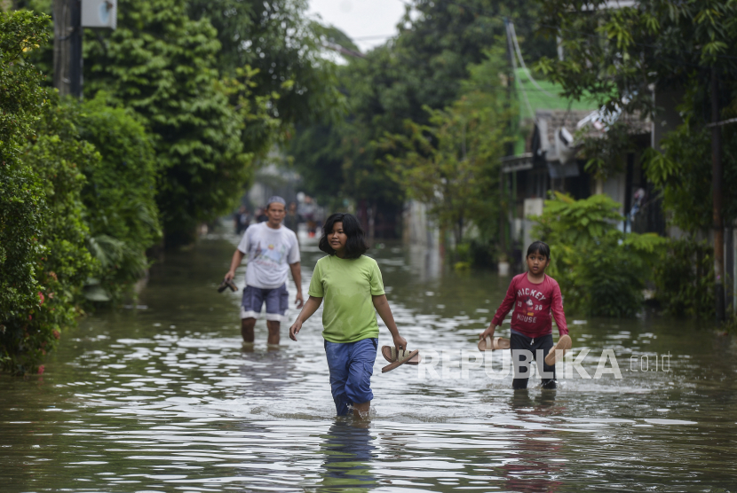 Warga berjalan di tengah banjir (ilustrasi). BPBD DKI Jakarta memantau perkembangan genangan air menyusul kenaikan status Pintu Air Pos Angke Hulu.