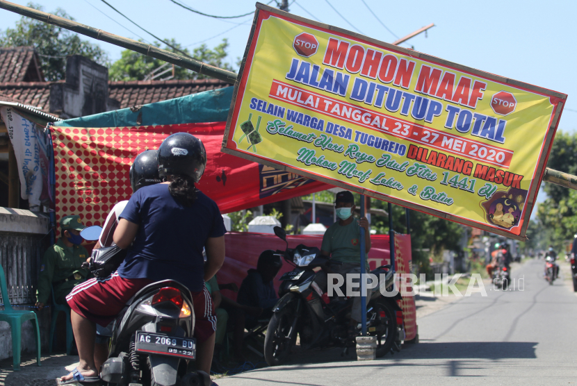 Pengendara melintasi portal dengan penjagaan petugas linmas di Desa Tugurejo, Kediri, Jawa Timur, Sabtu (23/5/2020). Sejumlah desa di Kediri menutup akses masuk wilayahnya untuk mengantisipasi warga luar desa berkunjung saat lebaran guna menangkal penyebaran COVID-19