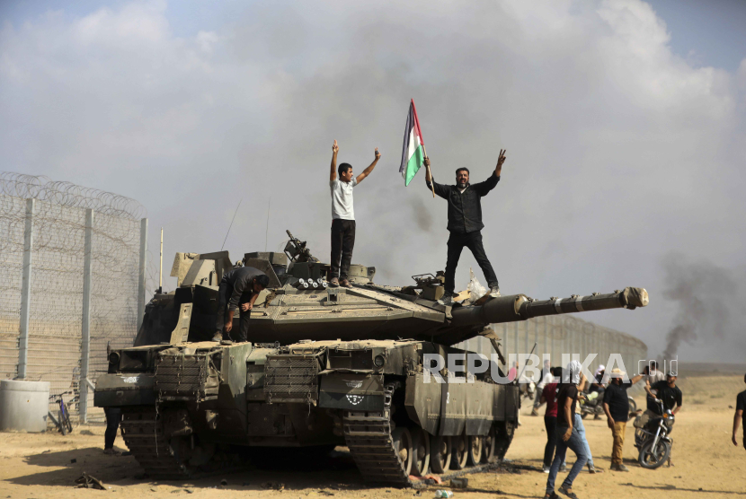 Warga Palestina mengibarkan bendera nasionalnya dan merayakannya dengan tank Israel yang hancur di pagar selatan Jalur Gaza di timur Khan Younis pada Sabtu, (7/10/2023).