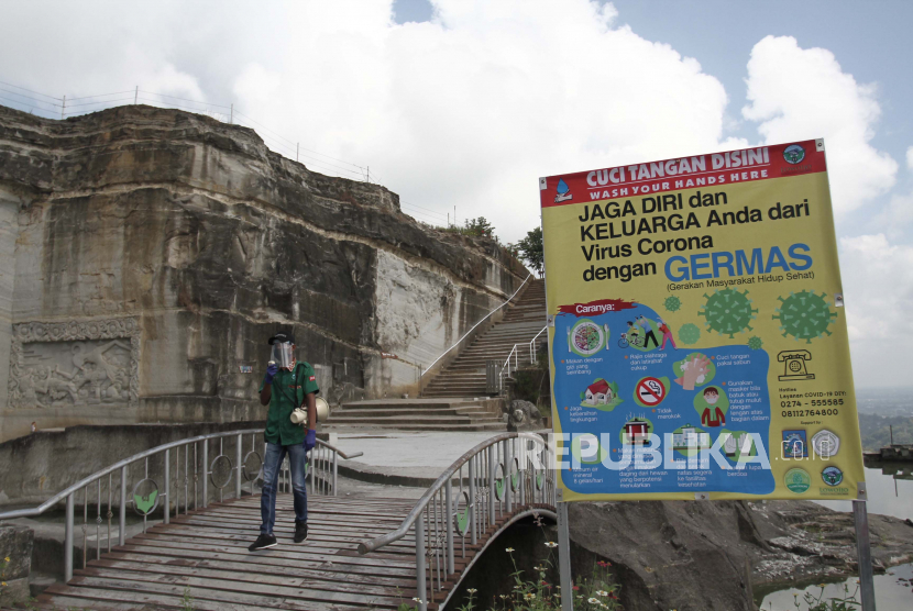 Pemandu wisata melintas di samping papan pengumuman pencegahan COVID-19 di obyek wisata Tebing Breksi, Prambanan, Sleman, DI Yogyakarta, Jumat (12/6/2020). 